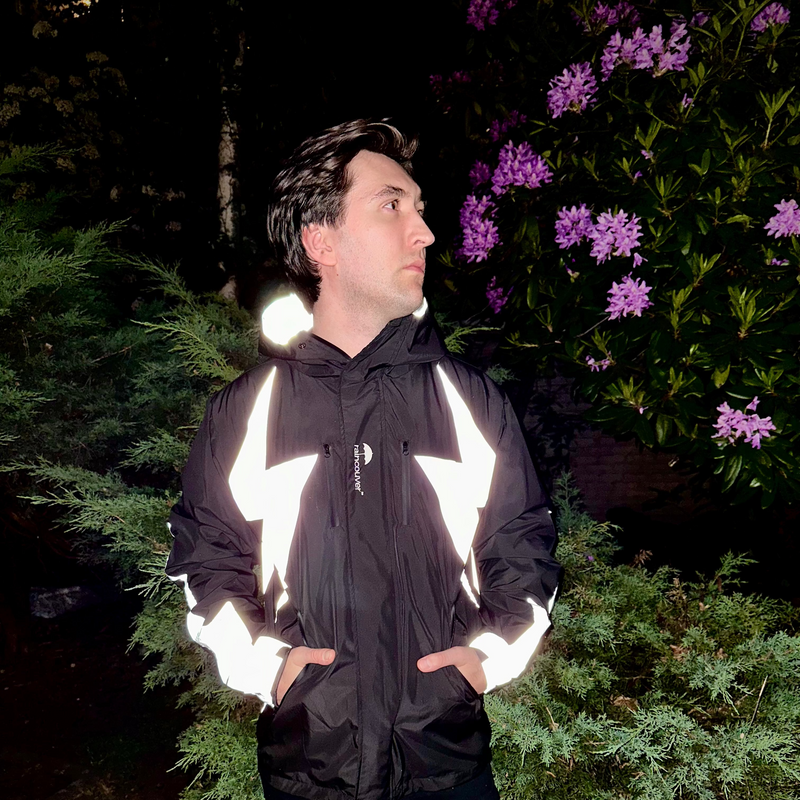 Person wearing a reflective black jacket standing outdoors with greenery and purple flowers in the background